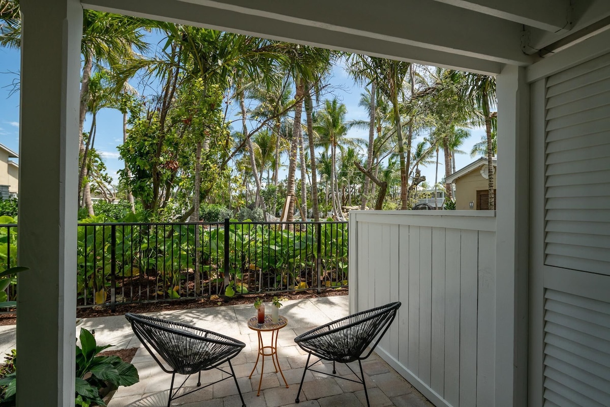 A covered patio with two black wire mesh chairs and a small round table.