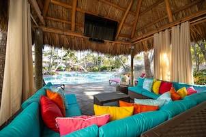 A covered outdoor seating area with a pool in the background.