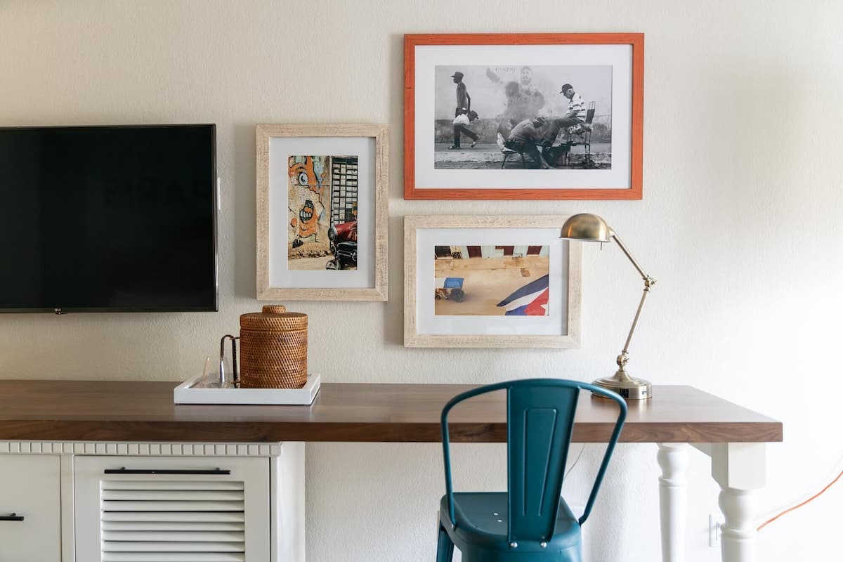 A room with a TV on the left, a desk with a lamp, and three framed pictures on the wall.