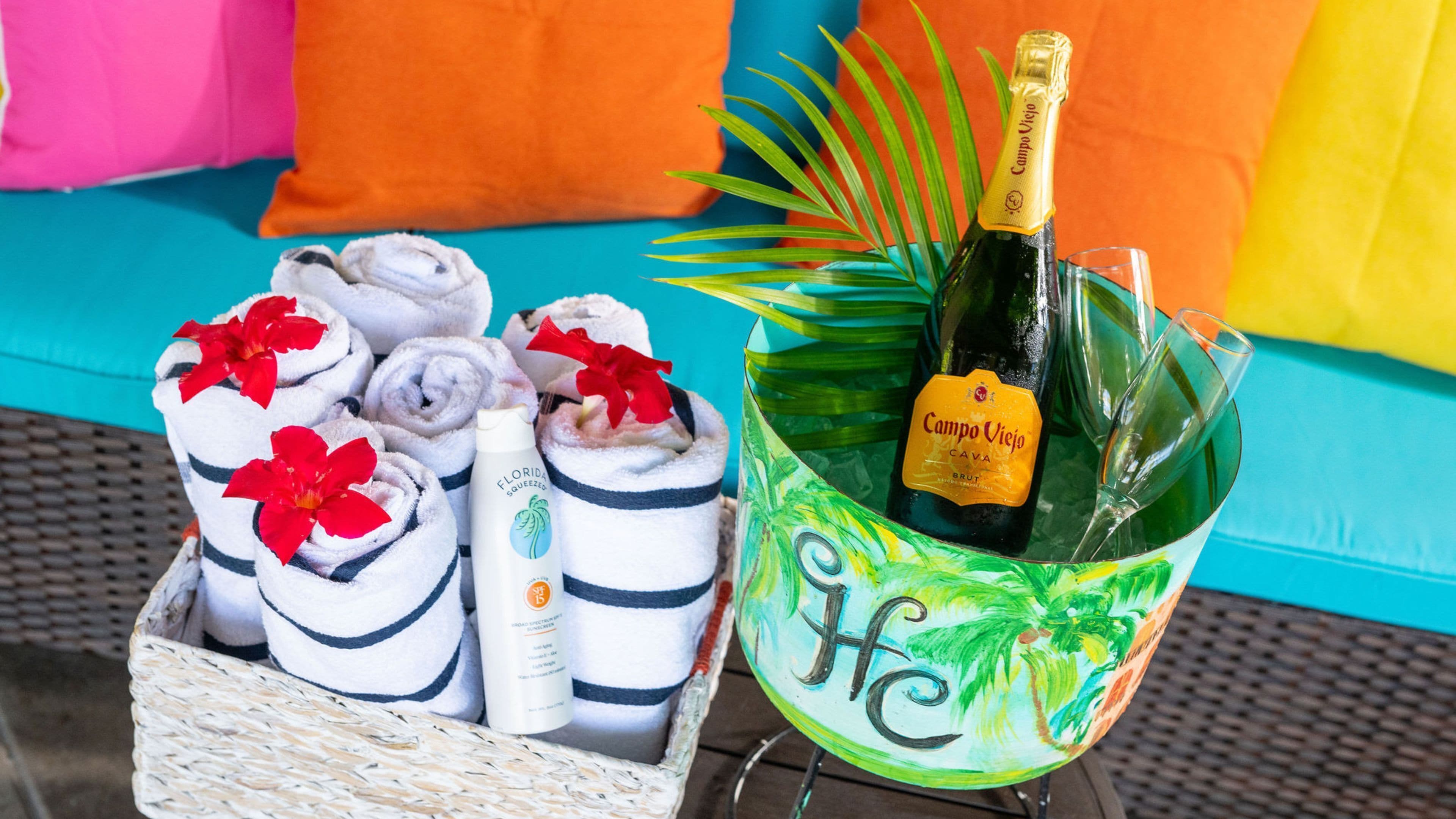 A wicker basket with rolled towels and a bottle of Campo Viejo Cava Brut, placed on a table with a colorful background.
