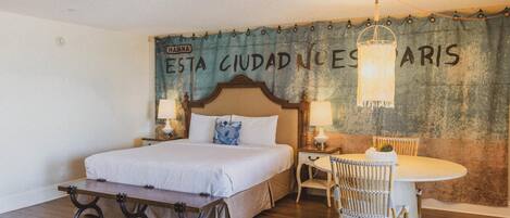 A hotel room with a bed, a table, and chairs. There is a curtain with text on the wall.