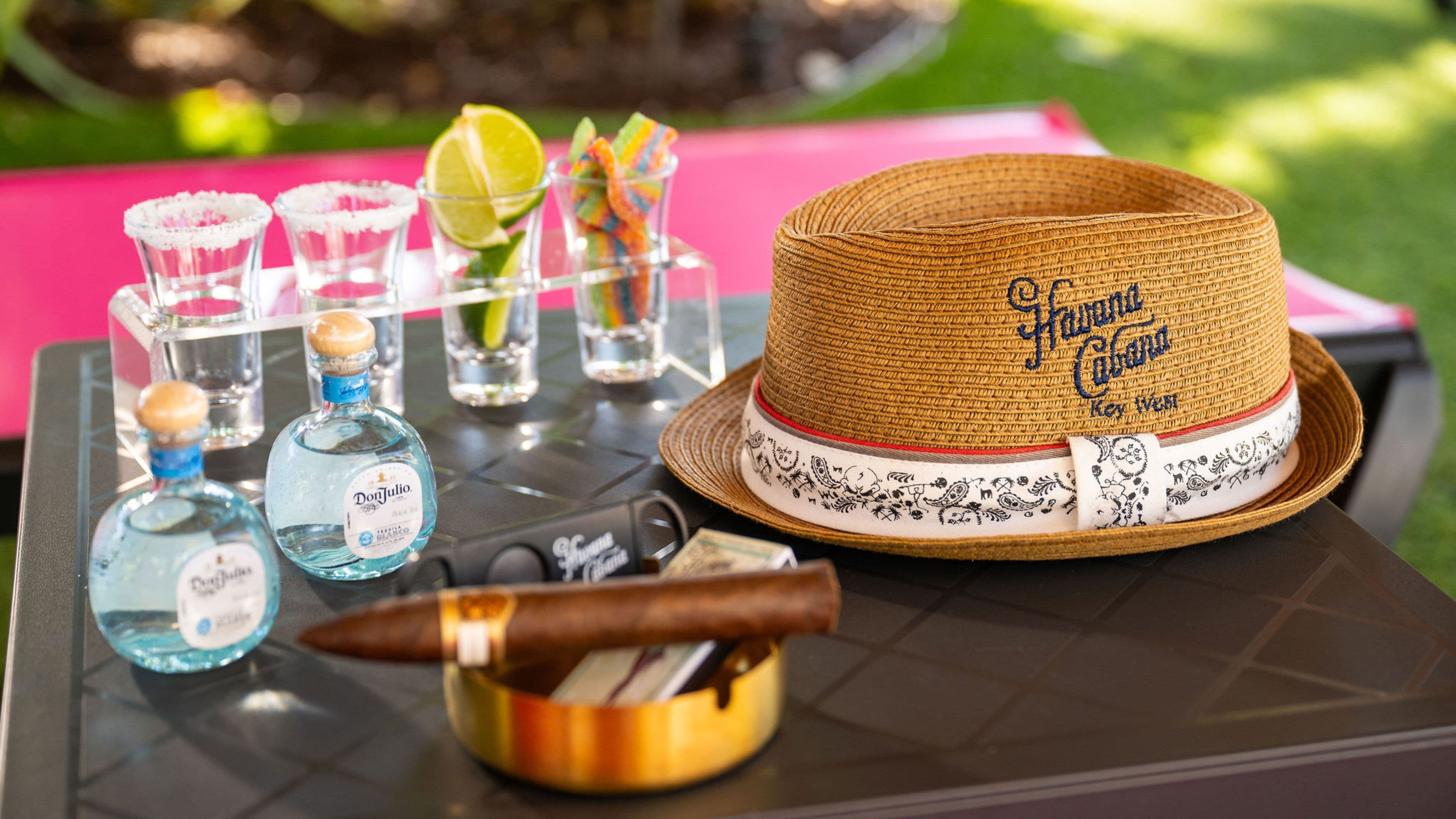 A table with a straw hat, shot glasses, bottles of Don Julio tequila, and a cigar.