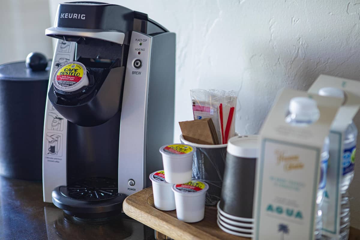A Keurig coffee maker with a coffee pod, a water dispenser, and disposable cups on a wooden surface.
