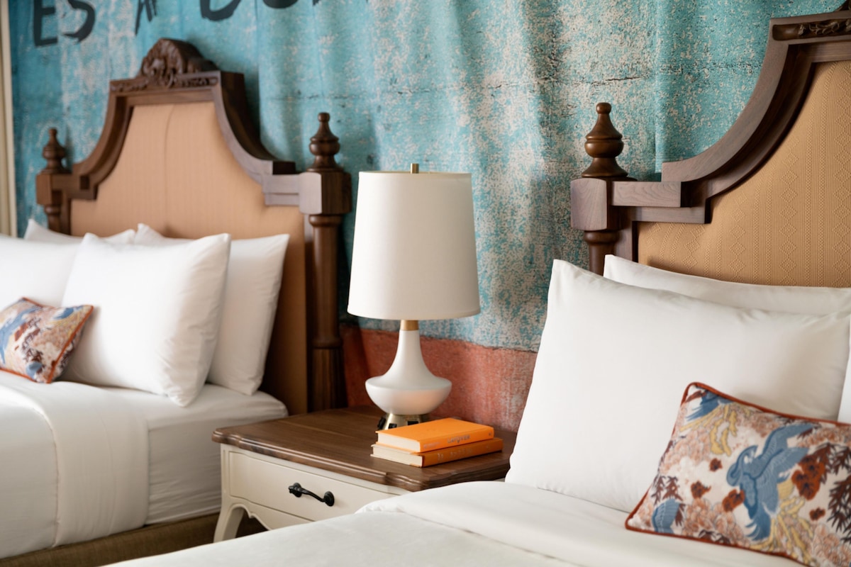 A hotel room with two beds, a nightstand with a lamp, and a wall with a decorative headboard.