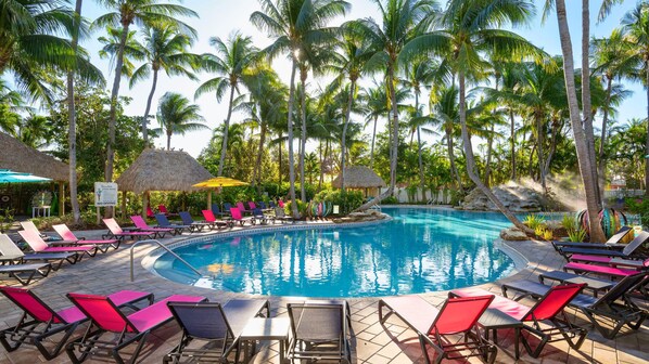 A pool area with lounge chairs and thatched umbrellas, surrounded by palm trees. - Havana Cabana at Key West (Key West)
