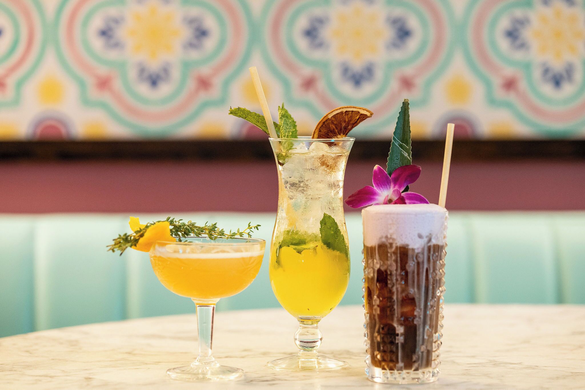 Three cocktails on a table with a colorful patterned background.