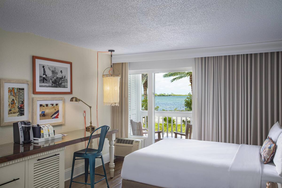 A hotel room with a bed, a desk with a chair, a coffee maker, and framed pictures on the wall.