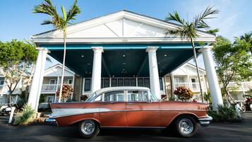 Classic car parked in front of a hotel with a symmetrical facade and tropical surroundings.