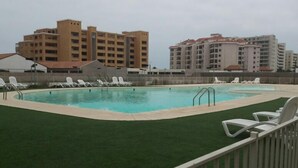 A swimming pool with white lounge chairs and a green lawn, surrounded by a white fence. - Depto Maria Aprilla 2 Piso (La Serena)