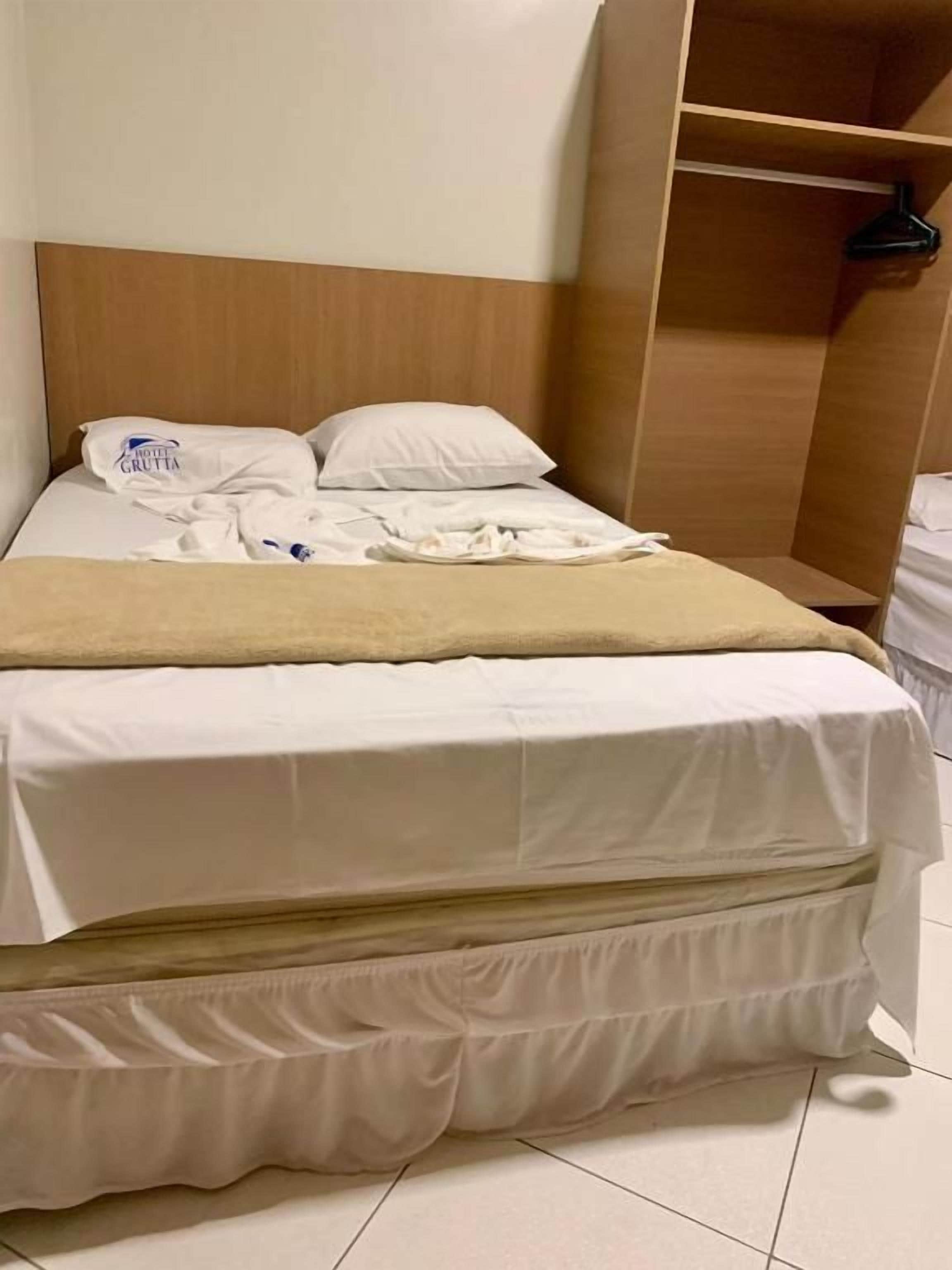 A hotel room with a bed, a wooden headboard, a closet with a hanging rack, and a white mattress.