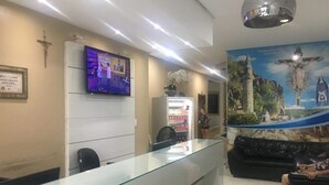 A reception area with a glass counter, a television mounted on the wall, a refrigerator, and a mural depicting a religious scene.