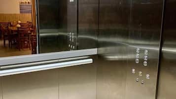 A metallic elevator interior with a reflective surface and a control panel with buttons.