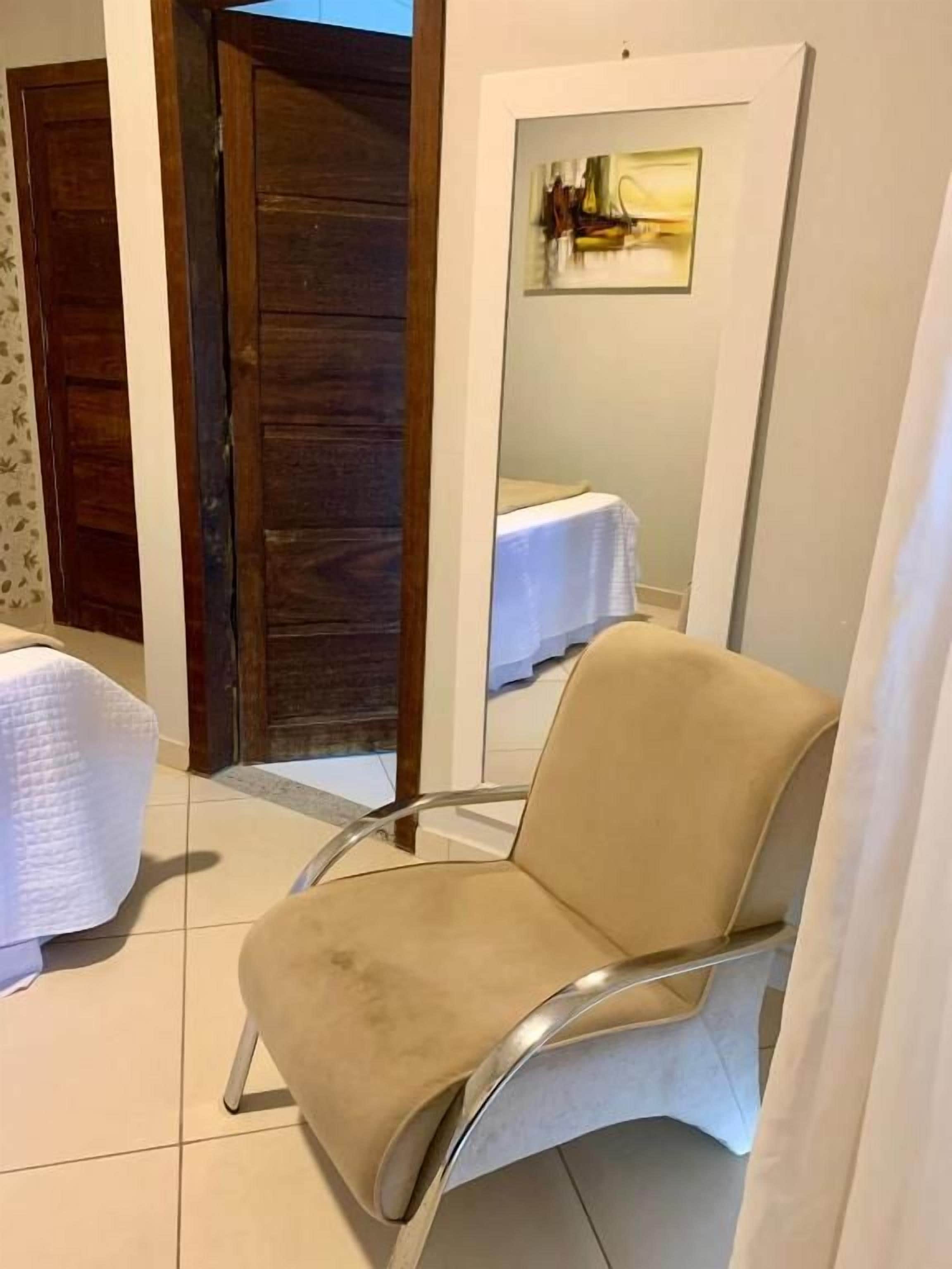Uma cadeira bege em um quarto com porta de madeira e parede branca com um quadro emoldurado.