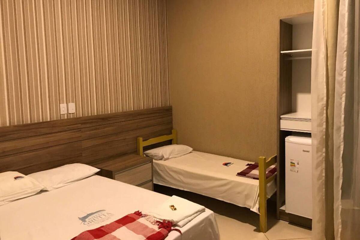 A small, compact room with two single beds, a wooden headboard, a small white refrigerator, and a striped wall.