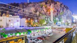 A nighttime view of a town with a prominent hill, a church with a lit tower, and a parking area with several cars.