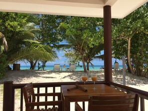 Eine Terrassenförmige Sitzgelegenheit am Strand mit Tisch und Stühlen, mit Blick auf einen Sandstrand und das Meer.