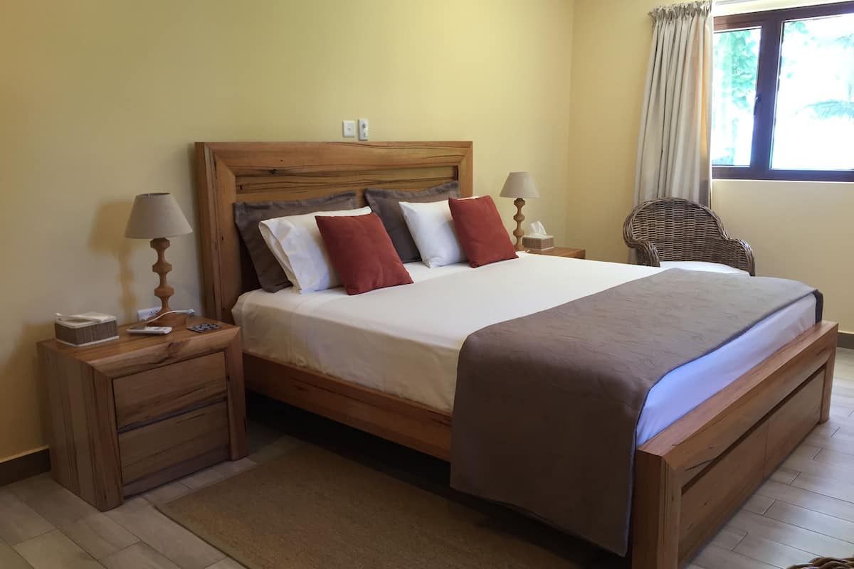 A wooden bed with a headboard, two bedside tables, a lamp, and a wicker chair.