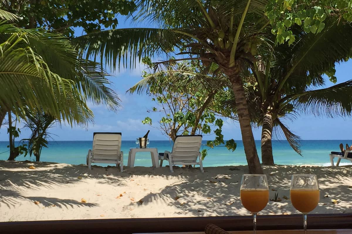 A beach view with two chairs and a table, a bottle, and two glasses of orange juice.