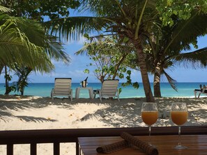 Vista de la playa con dos sillas, una mesa, una botella y dos vasos de jugo de naranja.