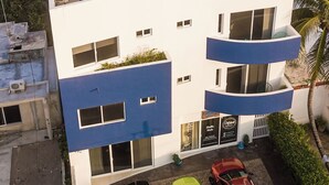 A modern building with a flat roof, multiple balconies, and a parking area with three cars. - Kaam Accommodations (Puerto Morelos)