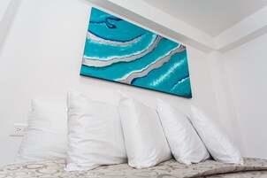 Un dormitorio con una cama, almohadas blancas y un cuadro abstracto colgado en la pared.