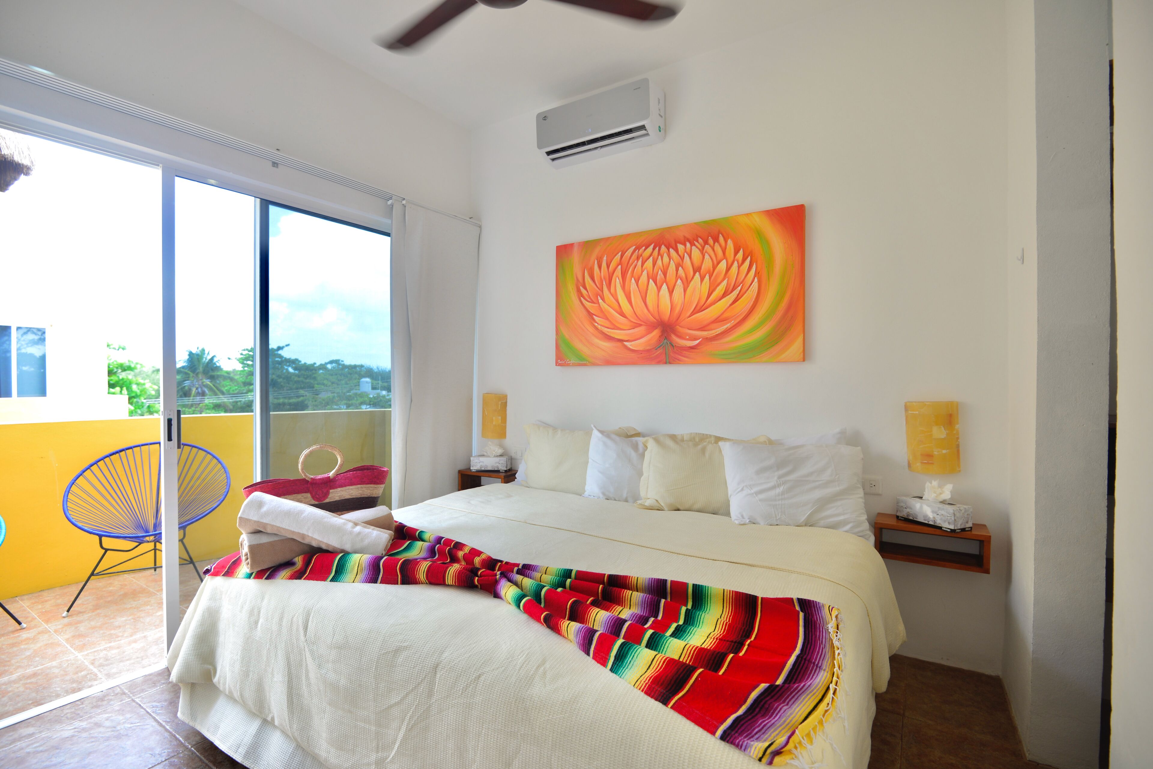 Un dormitorio con cama, una colcha colorida, un cuadro, una silla y una ventana.