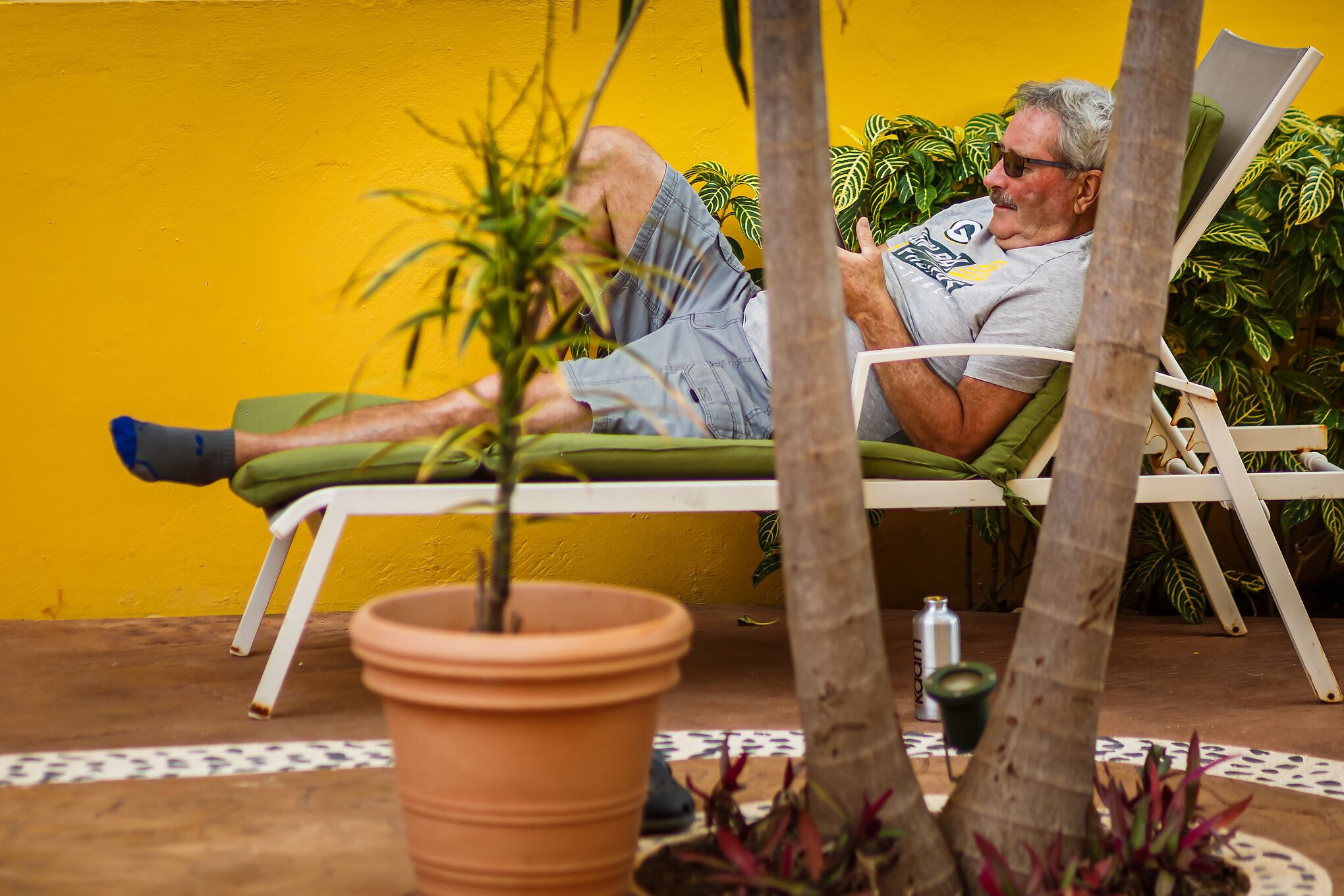 A man reclining on a white lounge chair with a yellow wall in the background.