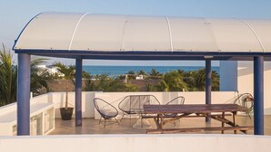 A covered outdoor seating area with a view of the ocean, featuring a table and chairs. - Kaam Accommodations (Puerto Morelos)