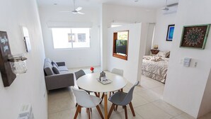 A modern living room with a grey sofa, a dining table with four chairs, and a small kitchen area with a refrigerator. - Kaam Accommodations (Puerto Morelos)
