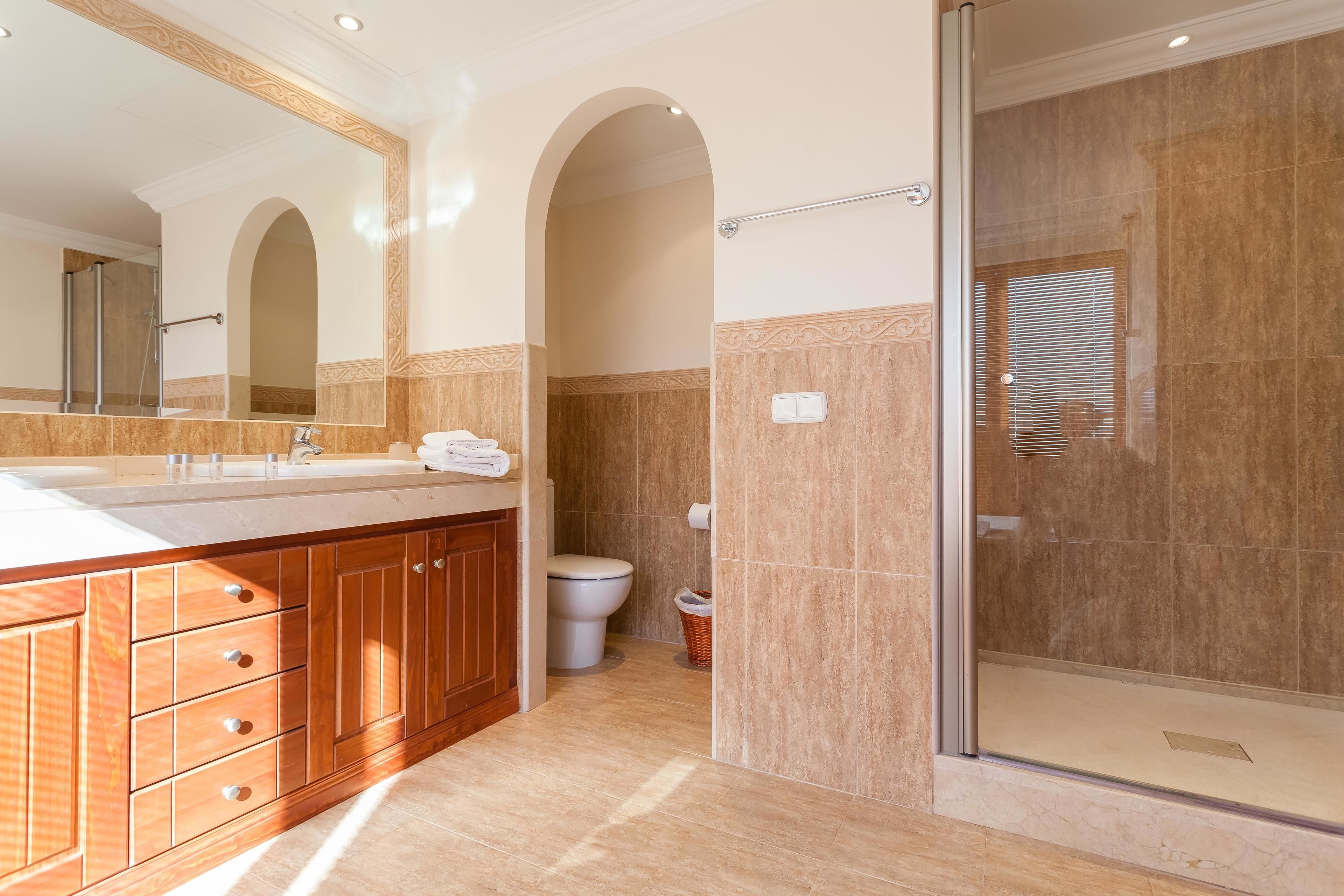 Une salle de bain moderne avec un grand miroir, un meuble-lavabo en bois, une cabine de douche en verre et des toilettes.
