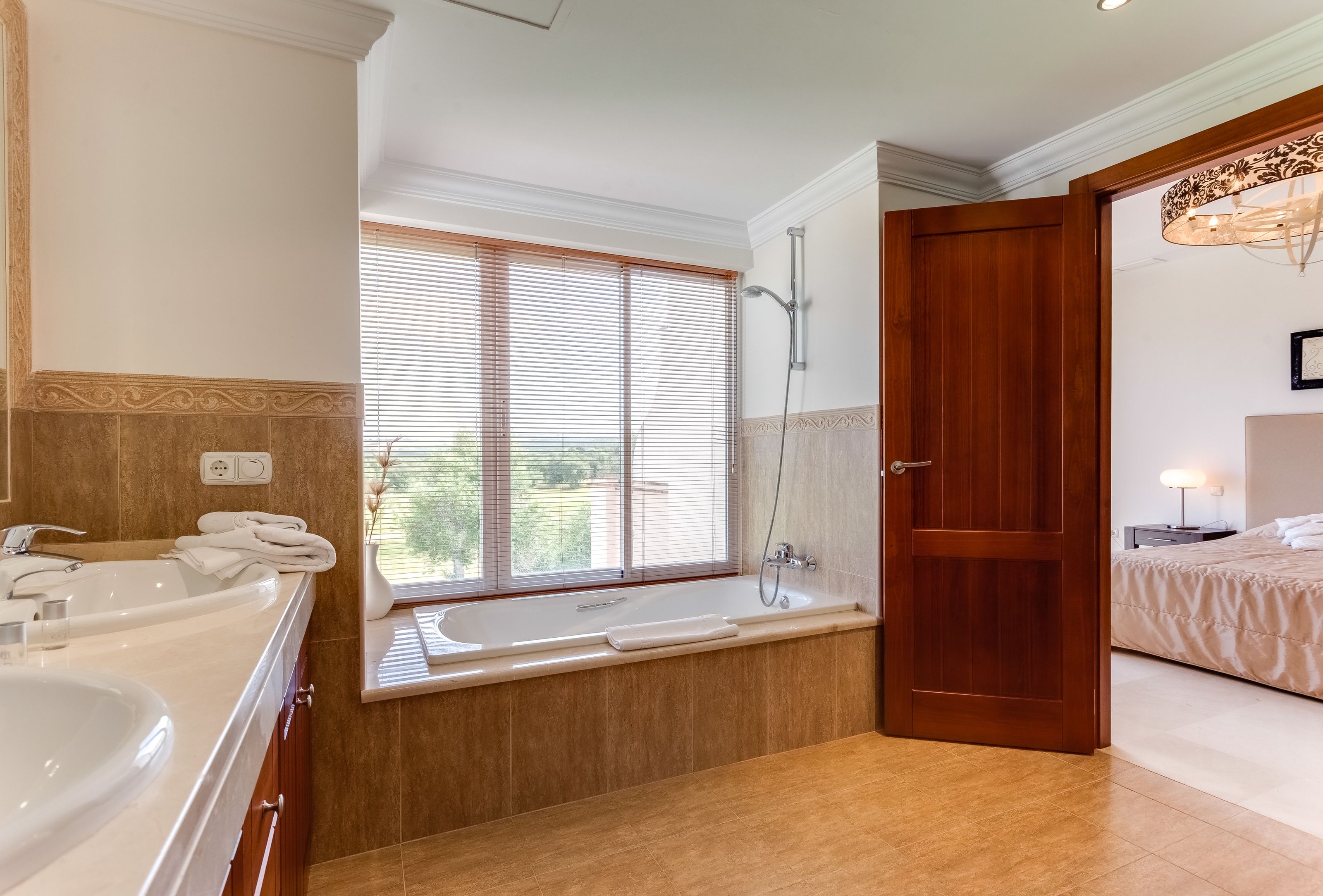 Un baño moderno con una bañera grande, ducha y ventana con persianas.