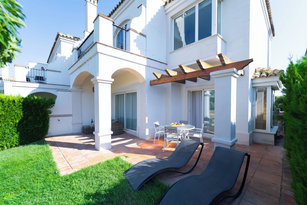 Una casa blanca con patio, mobiliario exterior y una pérgola.