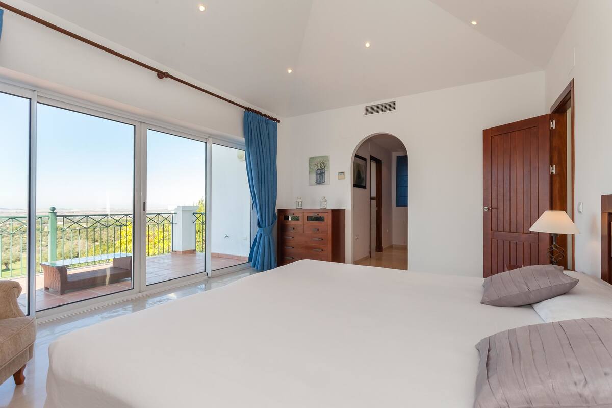 Un dormitorio con una cama grande, un aparador y un balcón con vistas.