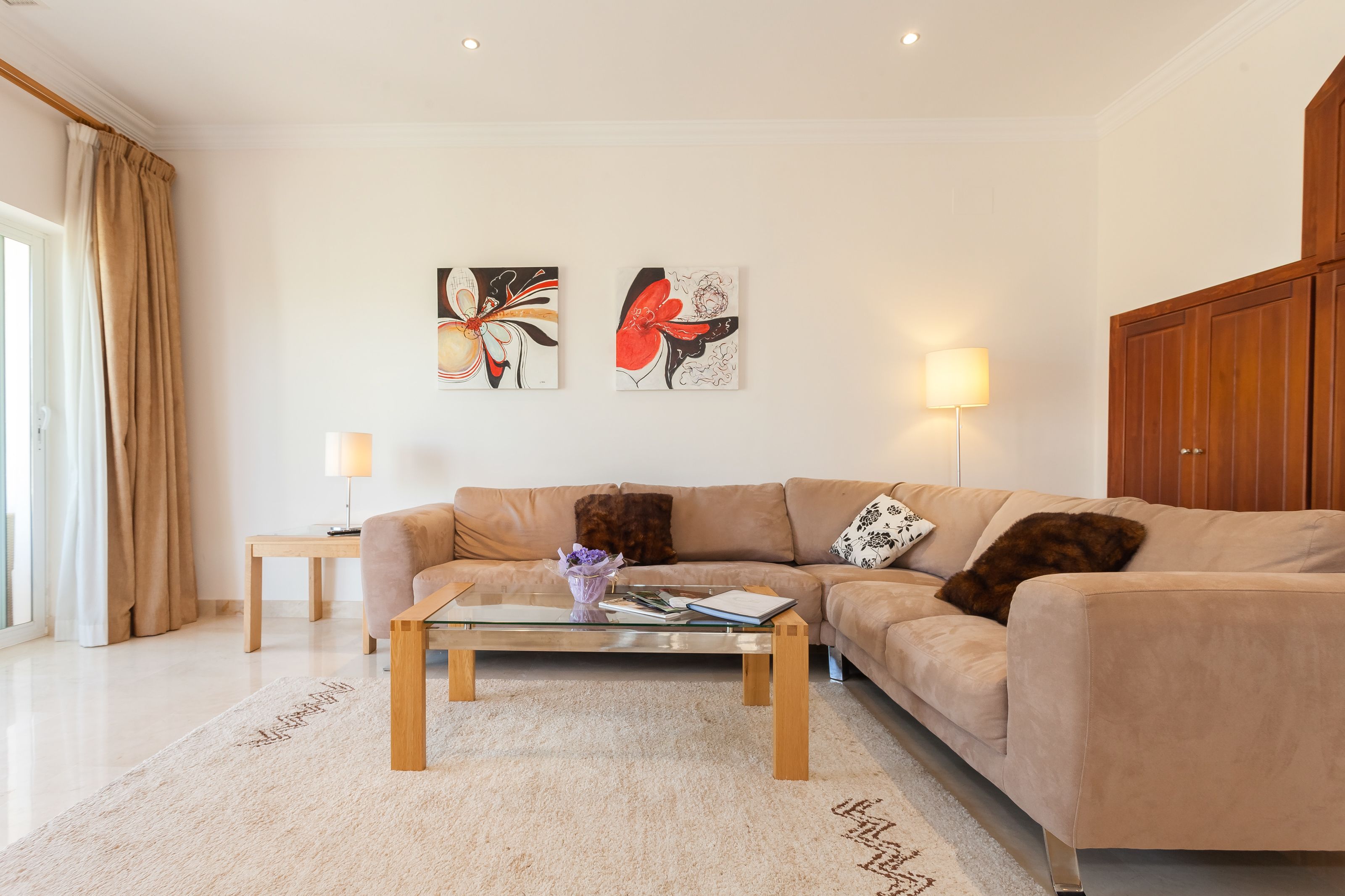 Een moderne woonkamer met een beige bank, een glazen salontafel en twee wandlampen.