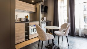 A modern kitchen with built-in appliances, a dining area with patterned chairs, and a large window with curtains. - CMG Tour Eiffel (Paris)
