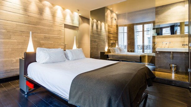 A modern bedroom with a large bed, bedside tables, a built-in shower, and a view of the city. - CMG Tour Eiffel (Paris)