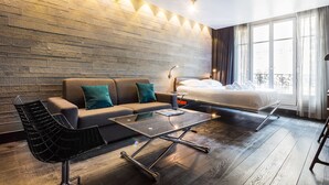 A modern hotel room with a sofa, a glass coffee table, a bed, and a view of the outdoors through large windows. - CMG Tour Eiffel (Paris)