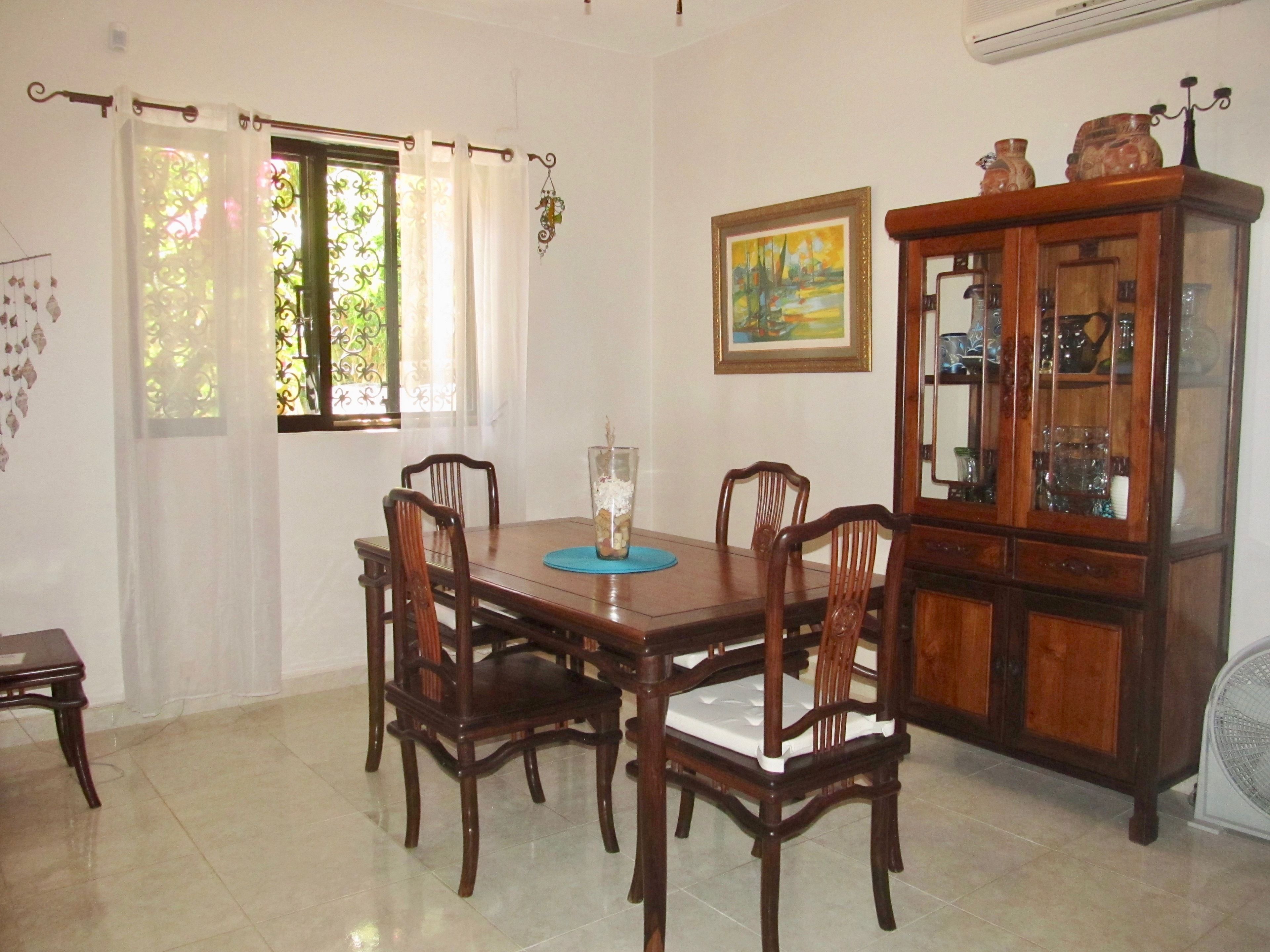 A dining area with a wooden table and chairs, a cabinet with glass doors, and a painting on the wall.