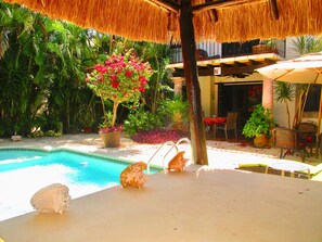 A pool area with a thatched roof, surrounded by lush greenery and potted plants. - Casa Royal Palms by Playa Paradise (Playa del Carmen)