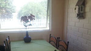 A dining area with a table set for two, a vase with flowers, and a window with a view of trees. - Casa en Bahia Inglesa (Caldera)
