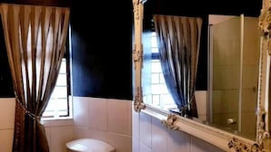 Ein Badezimmer mit Toilette, einem Spiegel mit aufwendigem Rahmen und Vorhängen an den Fenstern.