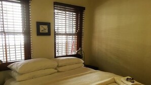 Ein Hotelzimmer mit Bett, Kissen, einem Bild an der Wand und einem Fenster mit Jalousien.