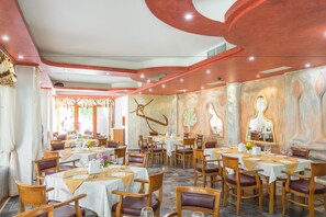 Ein Restaurant mit mehreren Tischen und Stühlen, ansprechend eingerichtet in einem großzügigen Speisesaal mit hoher Decke und Wanddekorationen.