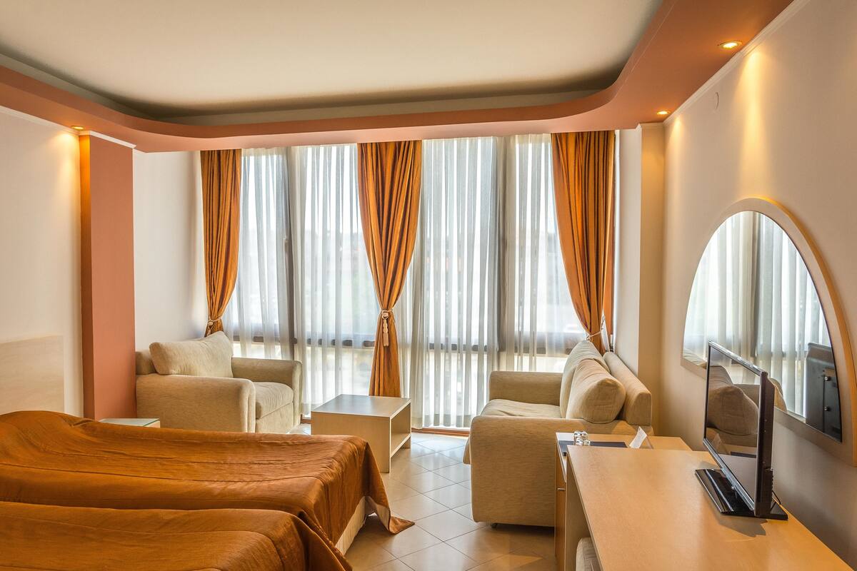 Une chambre d’hôtel avec deux lits, un canapé, une télévision et une fenêtre avec des rideaux.