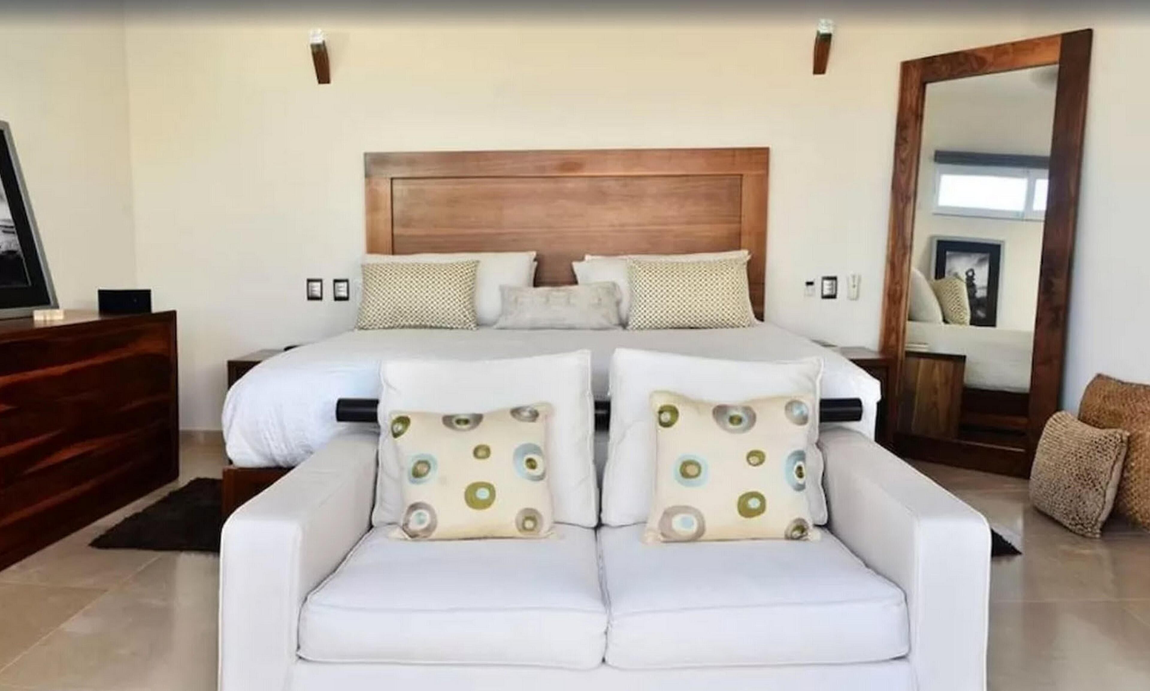 Ein Schlafzimmer mit einem großen Bett, einem hölzernen Kopfteil, zwei weißen Sofas und einem Spiegel.