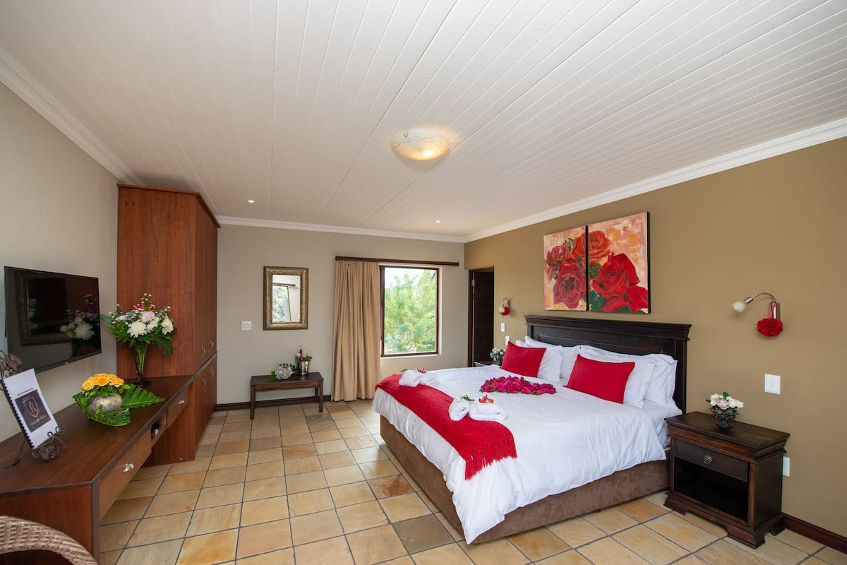 Een slaapkamer met een groot bed, een bureau, een stoel, een televisie en een raam.
