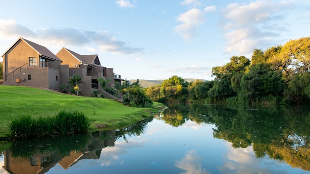 Una casa moderna con un jardín extenso y un lago tranquilo que refleja el cielo.