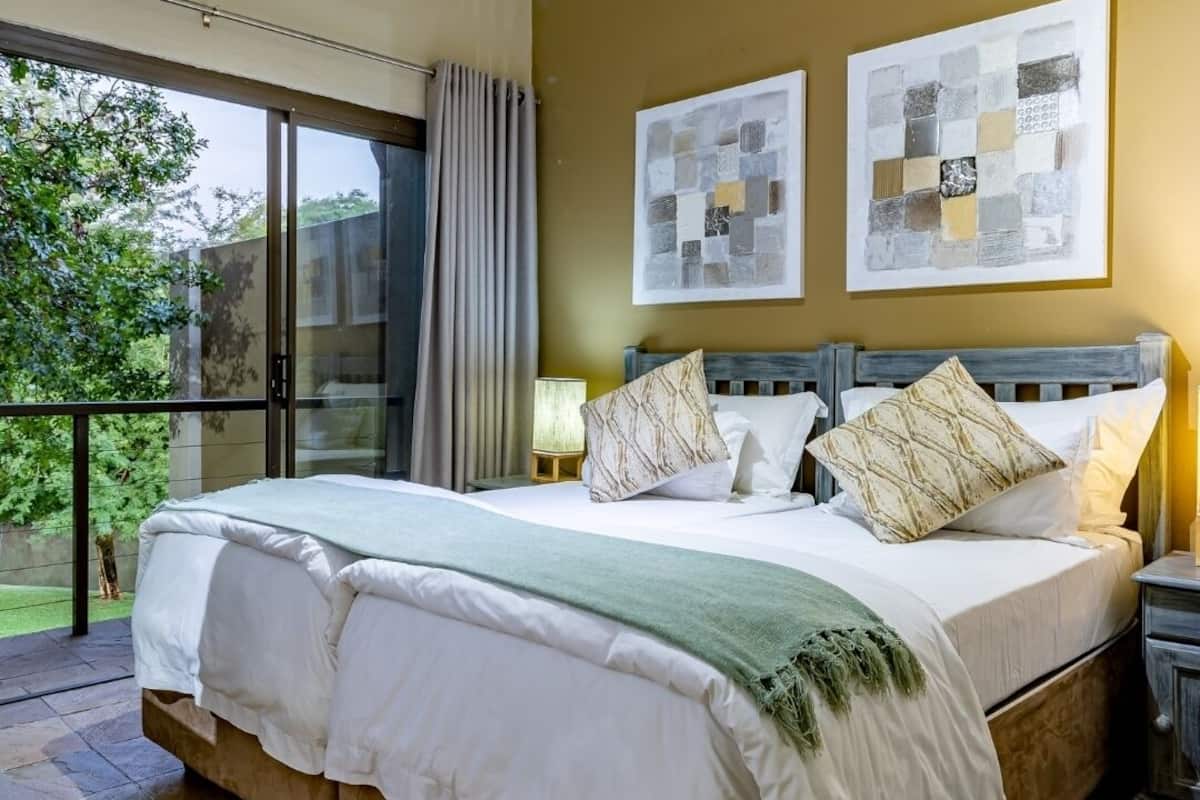 Een groot bed met een houten hoofdbord, wit beddengoed en meerdere kussens. Boven het bed hangen twee kunstwerken aan de muur.