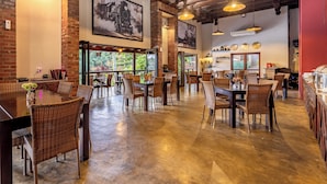 Un restaurante con paredes de ladrillo, vigas de madera y lámparas colgantes. Las mesas están dispuestas con sillas de mimbre y centros de mesa florales.