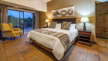 A hotel room with a large bed, two nightstands, a chair, a large window with curtains, and a brick wall.